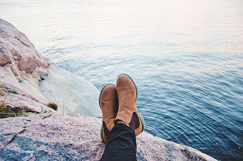 person sitting on gray rock beside body of water during daytime