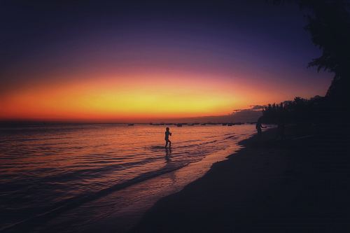 silhouette of person standing on shore during sunset