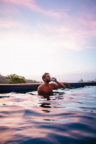topless man drinking beverage while on swimming pool