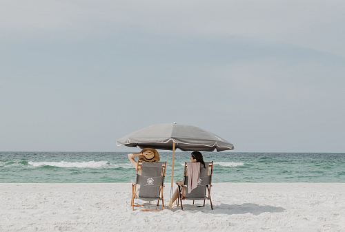 two people under beach umbrella near shoreline