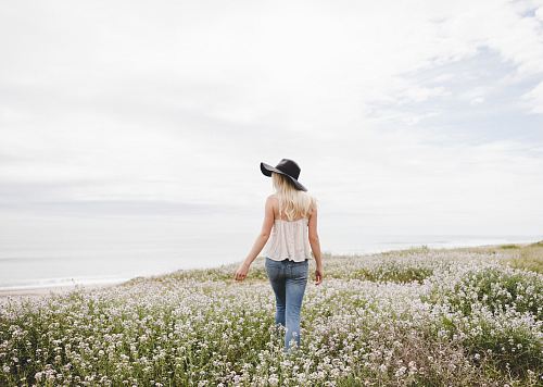 woman wearing black hat walking across the flower field during day time