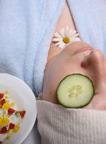 woman wearing blue robe lying with cucumber on eye