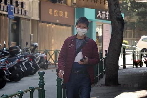 apparel man in red jacket standing beside green metal fence during daytime human