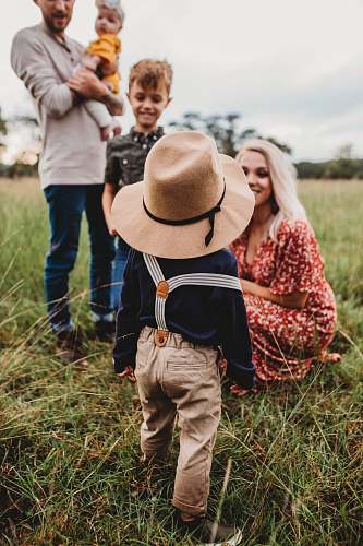 apparel woman sitting on grass while facing boy in brown hat clothing