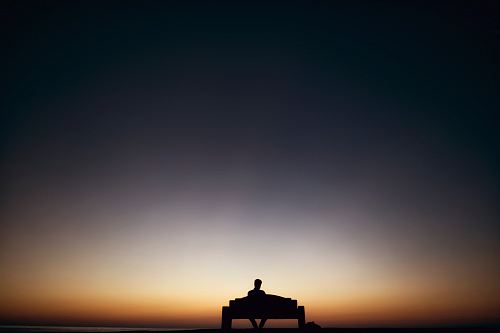 man sitting on bench facing sunset