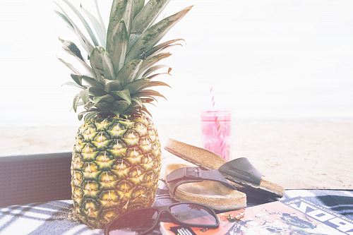 minimalist photography of pineapple near sandals and sunglasses