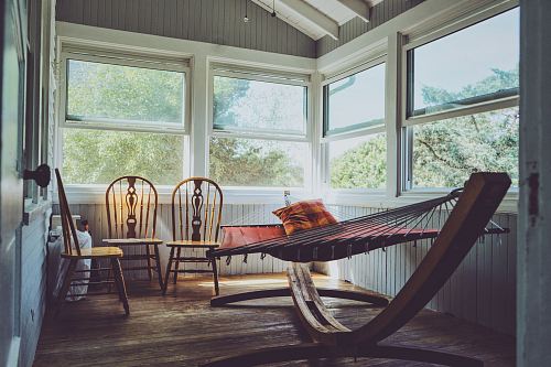 photography of grey, white, and brown wooden house interior with three brown wooden Windsor chairs beside brown hammock with glass windows