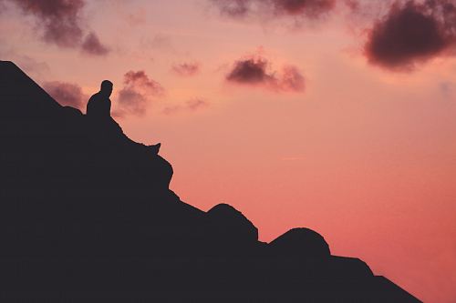 silhouette of man sitting on cliff