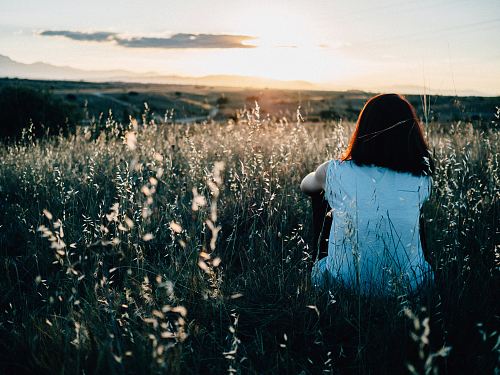 woman sitting on grass field watching sunset
