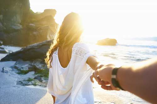 woman person holding woman's hand beside sea while facing sunlight couple