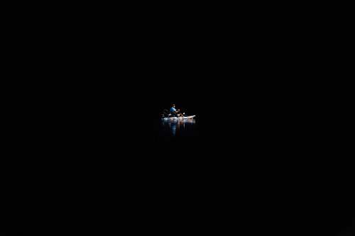 boat A person on a canoe in the water surrounded by complete darkness. background