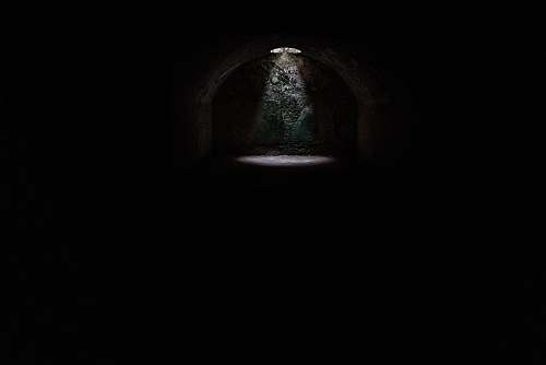black-and-white A spotlight coming from a hole in a dark underground cave in Minorca dark