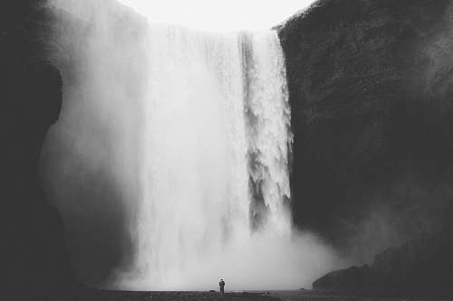 nature grayscale photo of man facing waterfalls grey