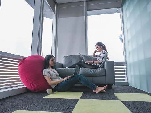 human two women sitting on sofa and floor inside gray painted room people